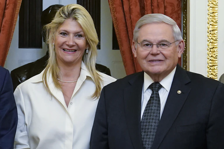 A smiling woman with dyed blonde hair standing next to a gray-haired man in a suit and tie.