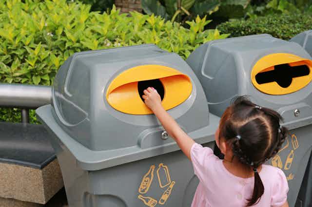 Anak perempuan menaruh sampah di tempat daur ulang
