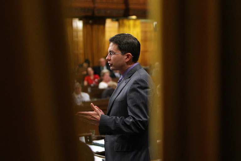 A man is seen through an open set of doors addressing Parliament.