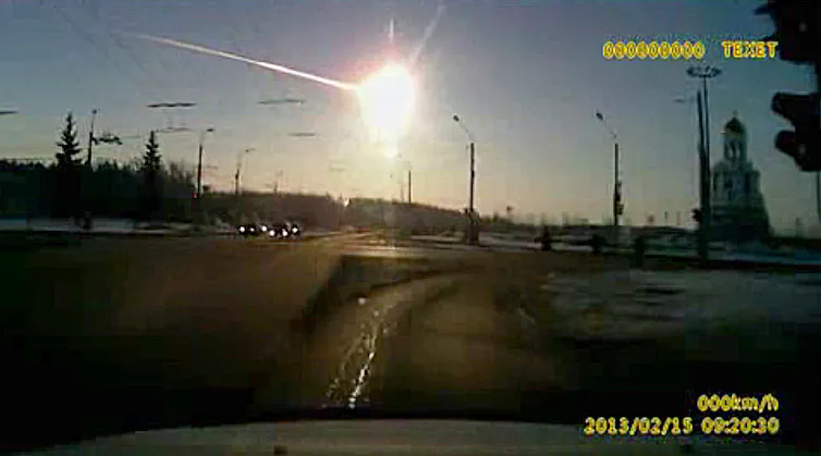 A screengrab from a dashboard camera video showing a bright fireball in the sky over a road.