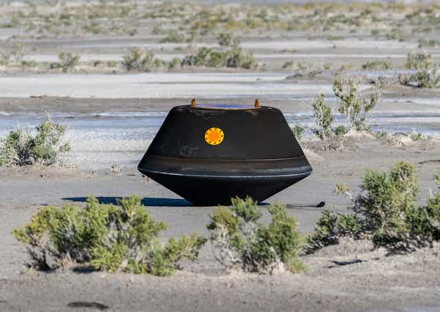 A charred, black capsule sitting in a desert landscape.