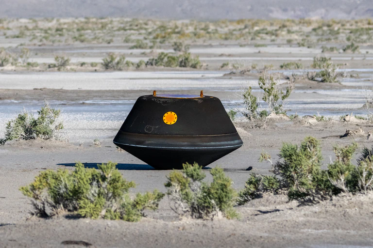 A charred, black capsule sitting in a desert landscape.