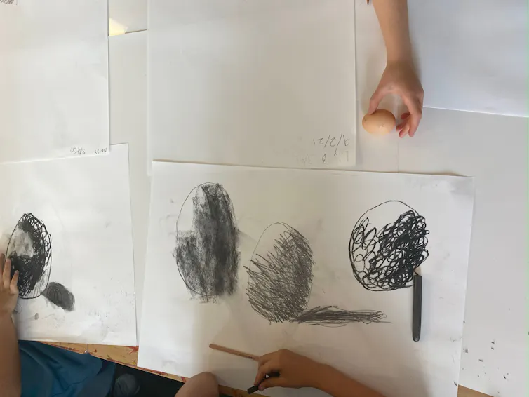 Students draw large pictures of an egg using charcoal.