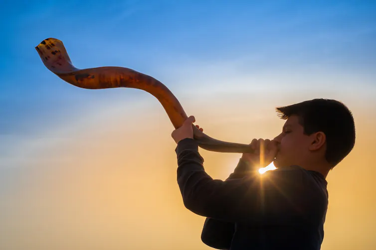 Teen boy blowing Shofar - ram's horn traditionally used for Jewish religious purposes.