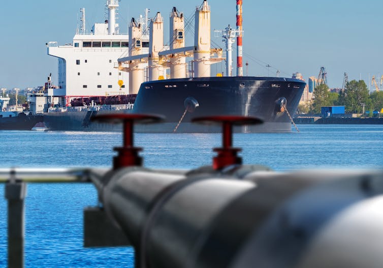 A large ship in port seen from the surface of an oil pipeline.