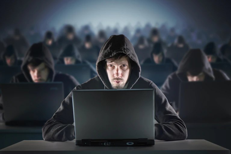 dozens of men wearing black hoodies sitting in front of laptops.