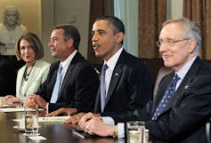 Sur une photographie de 2011, Barack Obama et John Boehner sont vus assis à une table dans la salle du Cabinet de la Maison Blanche.  Boehner a un léger sourire ;  Obama, sur le point de parler, a une expression de satisfaction.