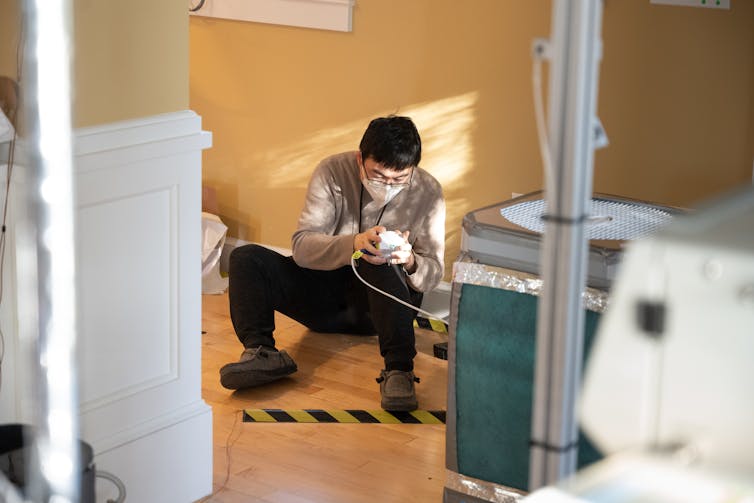 A young scientist, wearing a face mask, and a large air purifier.