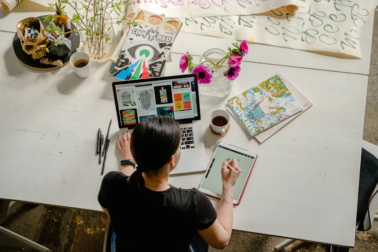 A woman works at a desk with magazines, a tablet and coffee.