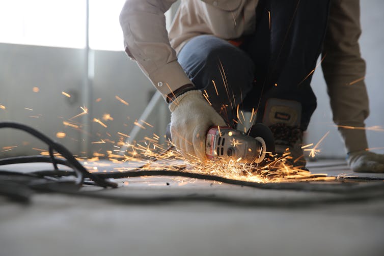 A worker uses a grinder on the floor, surrounded by cables.
