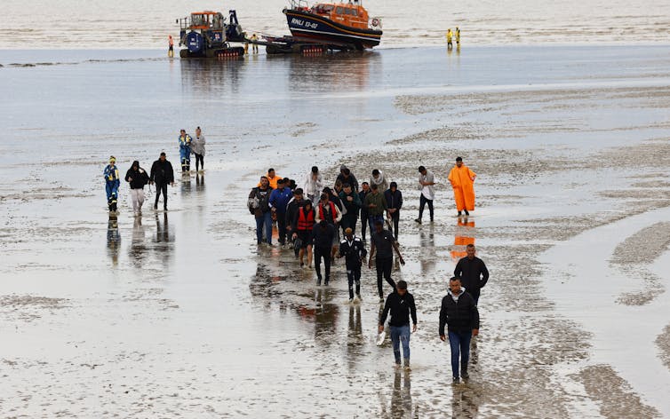 Asylum seekers walking ashore on a beach after leaving an RNLI rescue vessel