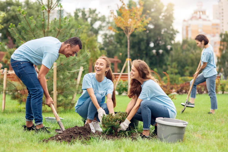 Young people planting trees and digging ground with a shovel.
