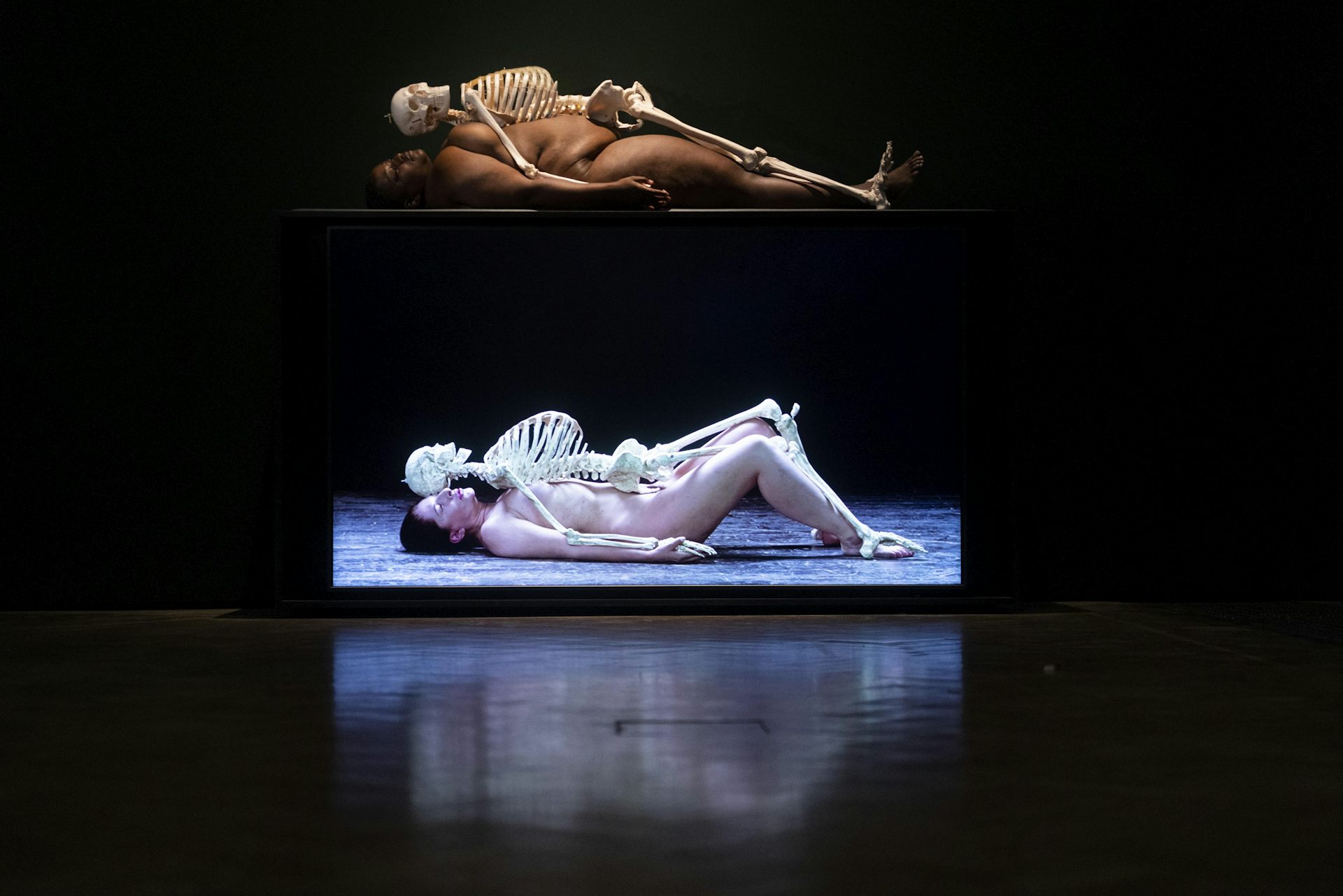 Two screens showing Abrambovic and another woman separately lying underneath skeletons