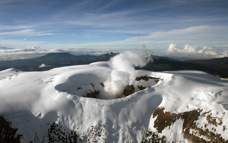 A mountainous scene with a large smoking crater covered in snow.
