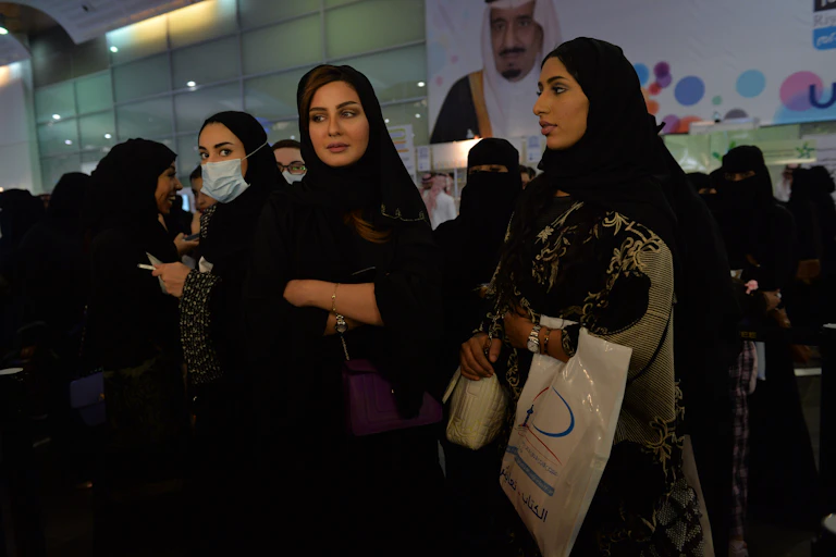 Several women standing in a group wearing a loose-fitting, long, black garment that covers their bodies, along with a head covering.