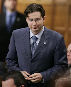 A young man with dark hair and a blue suit stands in the House of Commons.