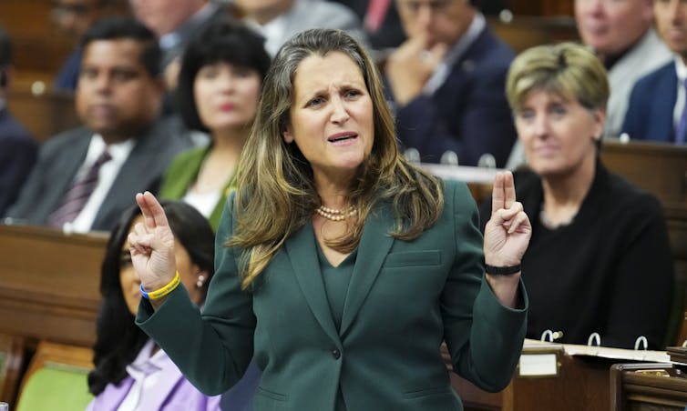 A woman in a green jacket looks irritated as she gestures while speaking.