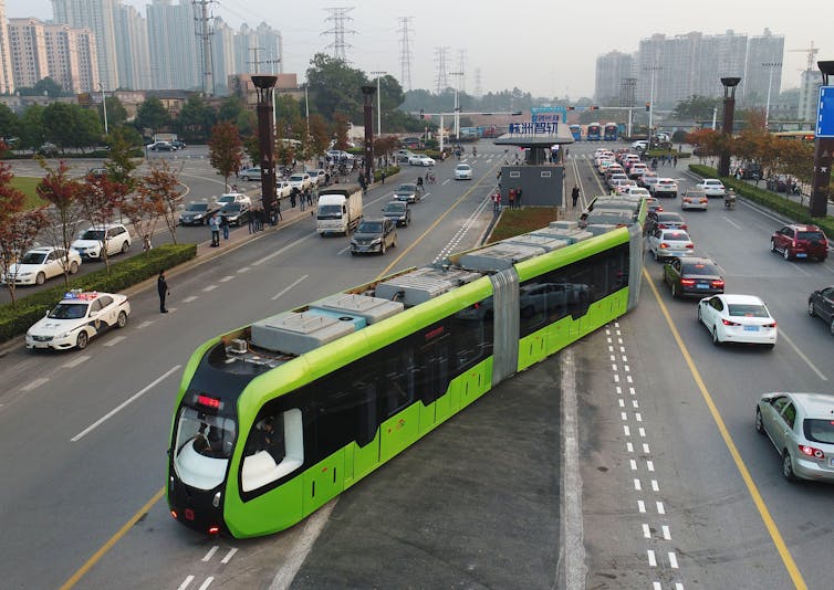 A green trackless tram in the middle of two major urban roads