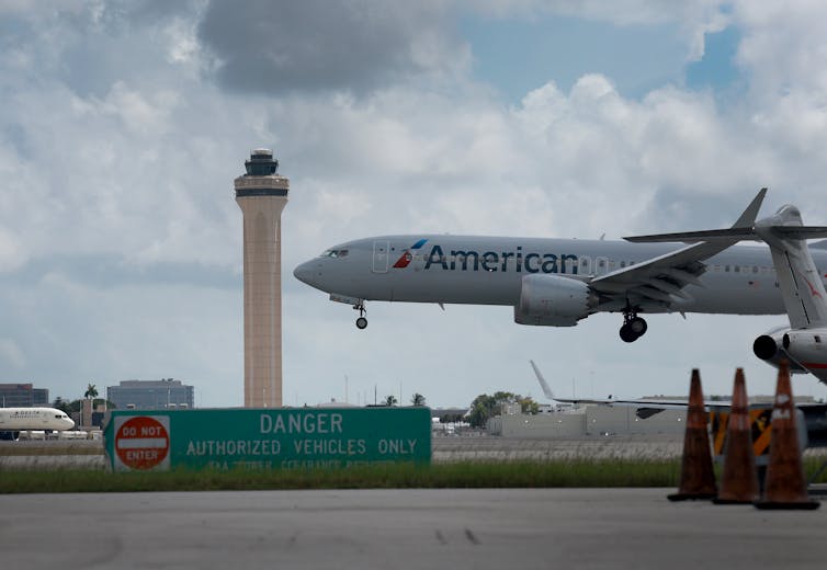 An airplane landing near an air traffic control tower.