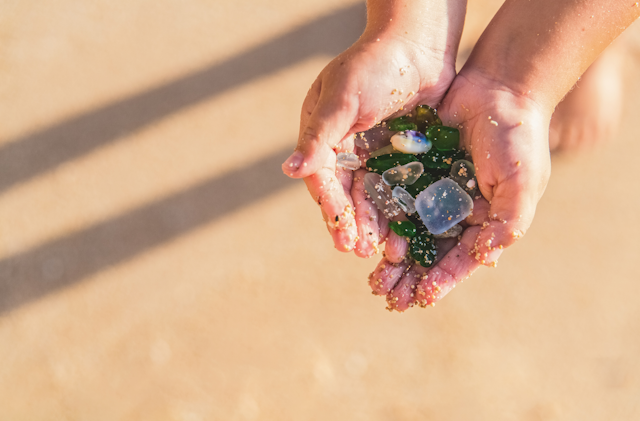 Hands hold pieces of clear and green beach glass
