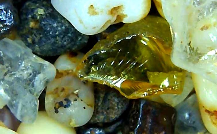 A zoomed in look at sand -- several small rocks of varying colors, from yellow to white to gray.