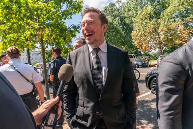Elon Musk rit en parlant à des journalistes