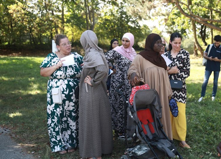 A handful of women in long dresses, and many with headscarves, stand and chat on the grass.