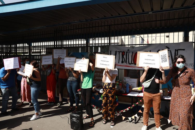 People at a protest stand beneath an awning as they hold signs over their faces.