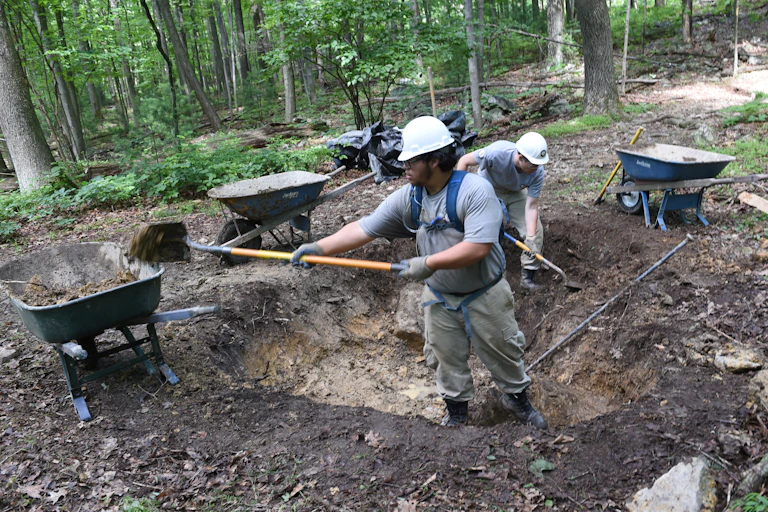 Two people dig dirt and debris.