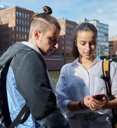 Two youth seen looking at a smartphone.