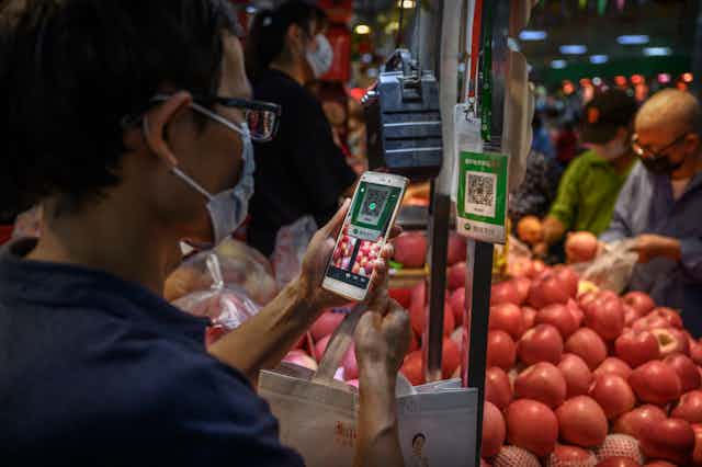 A man holds a smartphone up to a QR code in a produce market