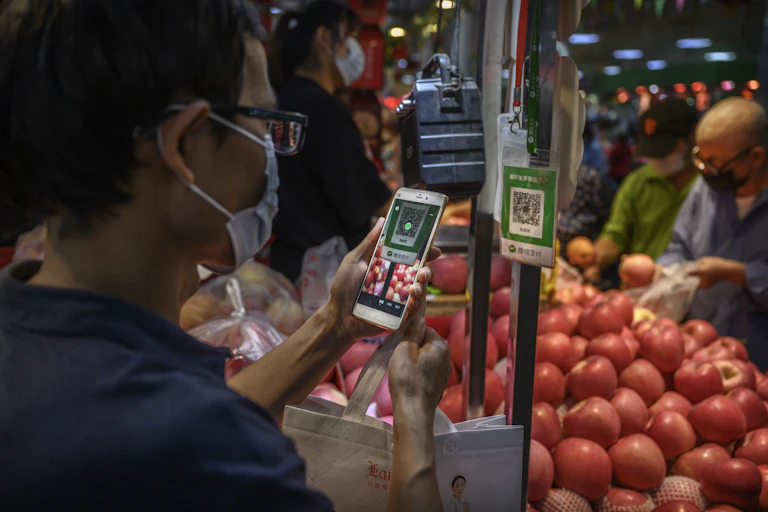 A man holds a smartphone up to a QR code in a produce market