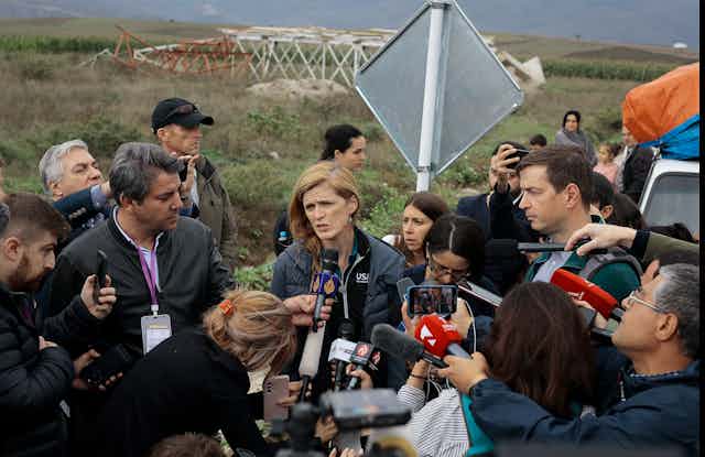 A woman speaks into a microphone surrounded by journalist.