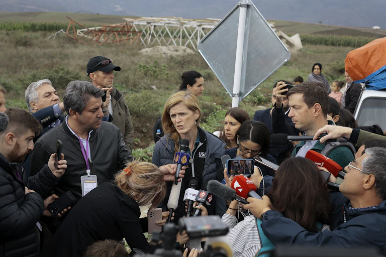 A woman speaks into a microphone surrounded by journalist.