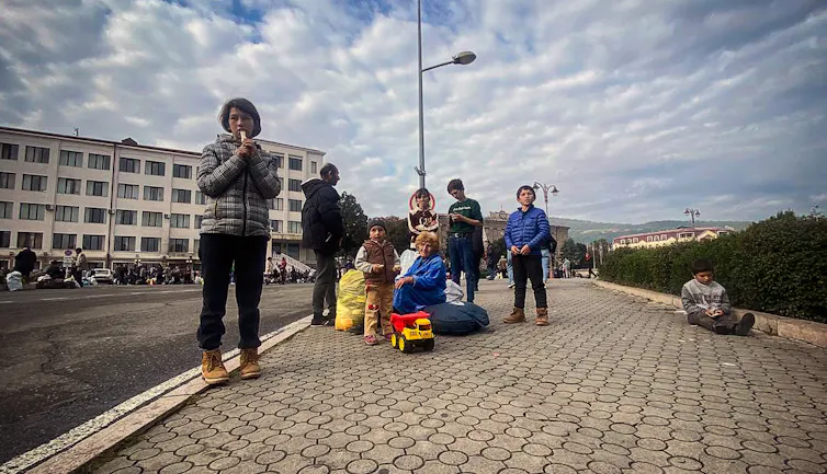 A group of people including children stand on a street