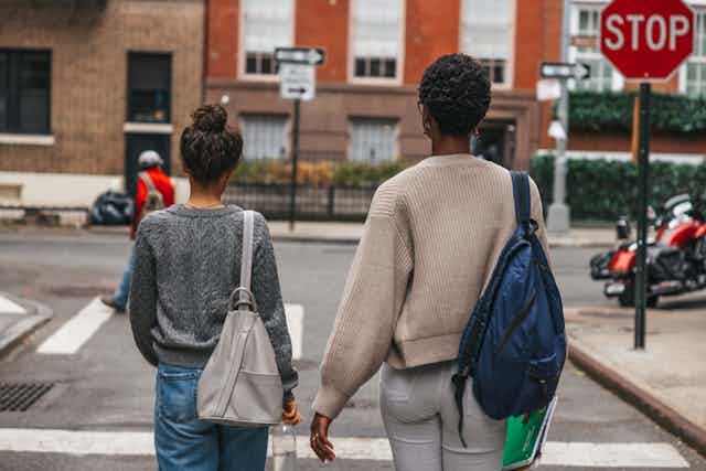 Woman and girl wearing backpacks walk down city street