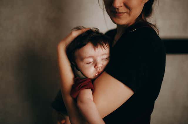 A mother holds a sleeping baby.