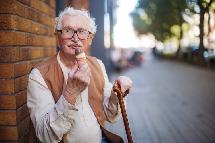 Older man eating icecream, sitting outside with walking stick