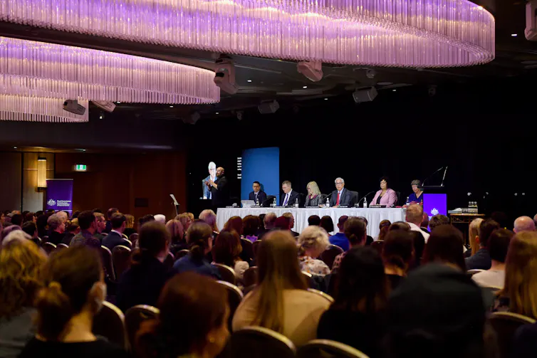 ballroom with panel of people at front and large audience seated