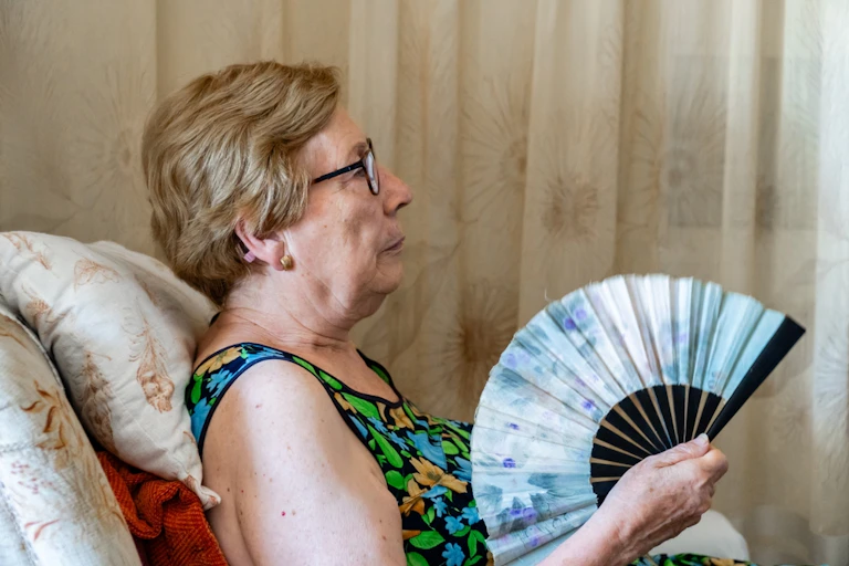 Older woman sitting in armchair fanning herself