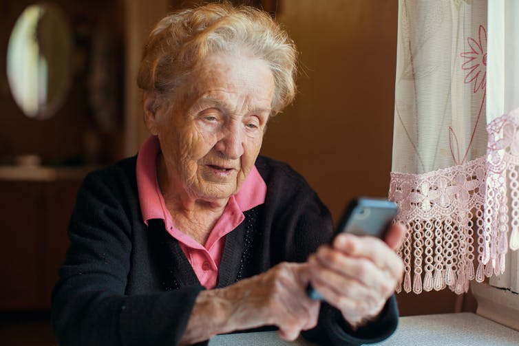 Older woman using smartphone at home, next to window