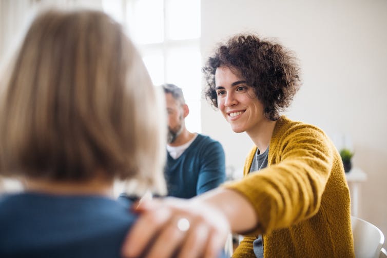 Counsellor or psychologist putting hand on shoulder of woman in group therapy