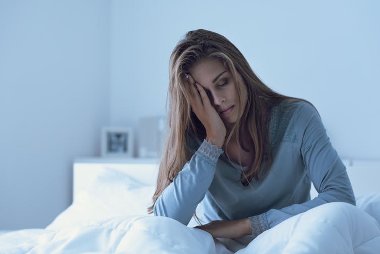 A fatigued woman sits in her bed.