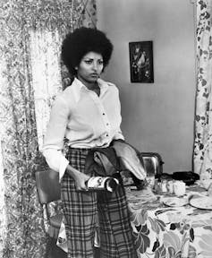 A black women in her home wielding a glass bottle to protect herself.