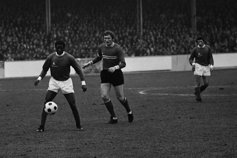 Three men in sportswear look at a ball on a football ground
