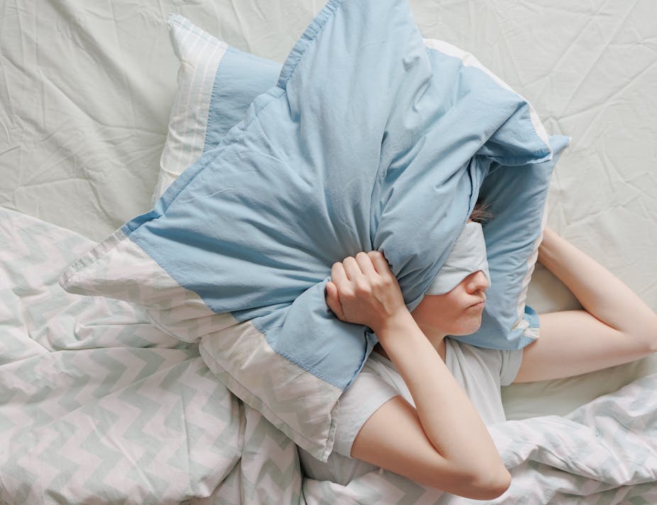 Mujer tapándose la cabeza con almohadas intentando dormir.