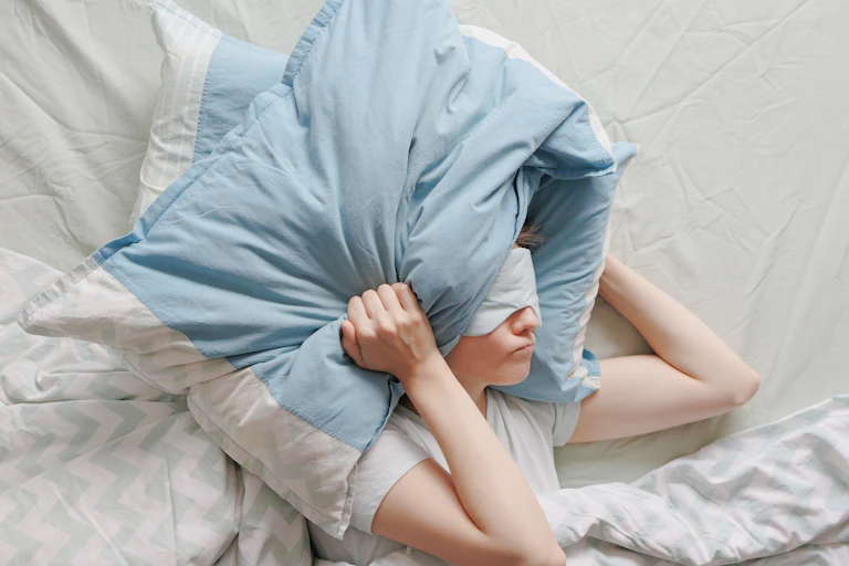 Mujer tapándose la cabeza con almohadas intentando dormir.