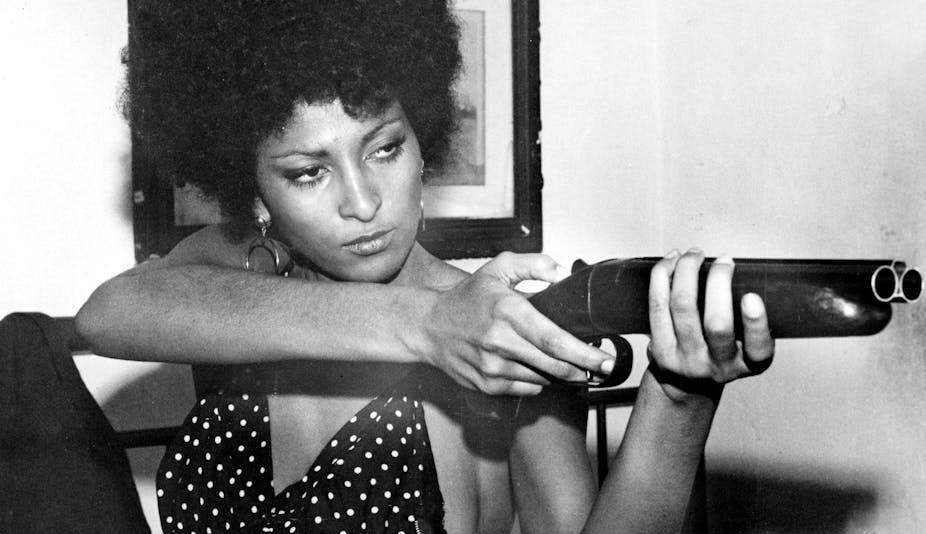 A black woman, eyes narrowed, holding a sawn-off shotgun. 