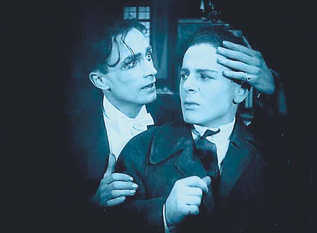 a black and white film still where one man places his hand around another's forehead