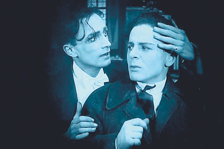 a black and white film still where one man places his hand around another's forehead